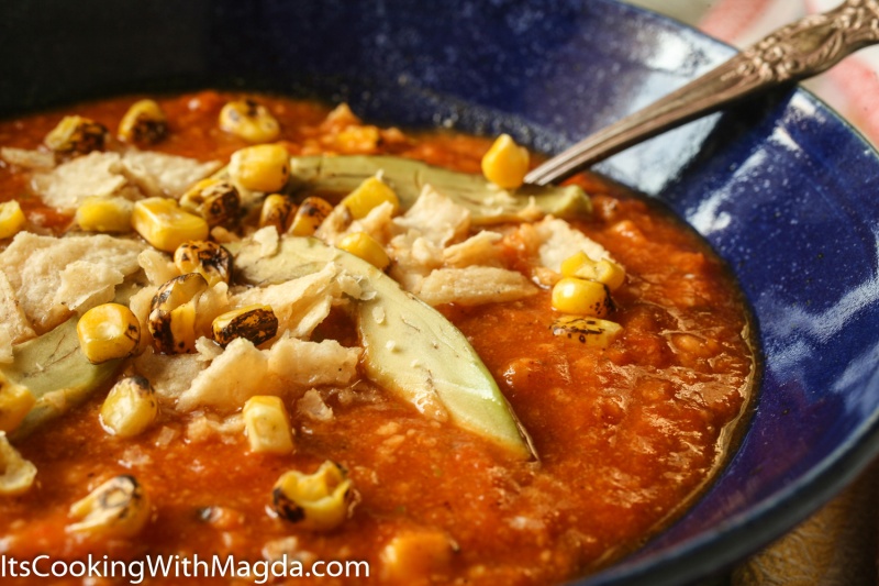 tortilla soup with roasted corn , avocado and chips on top