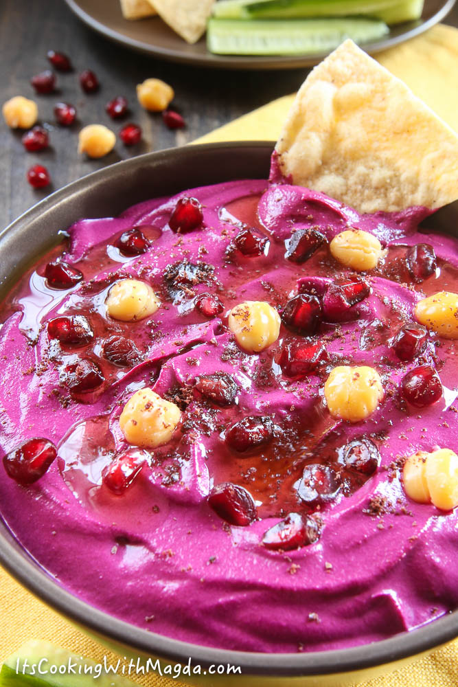 beet hummus in a brown bowl decorated with chickpeas and pomegranate