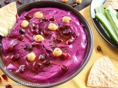 a bowl of beet hummus decorated with chickpeas, pomegranate seeds and sumac