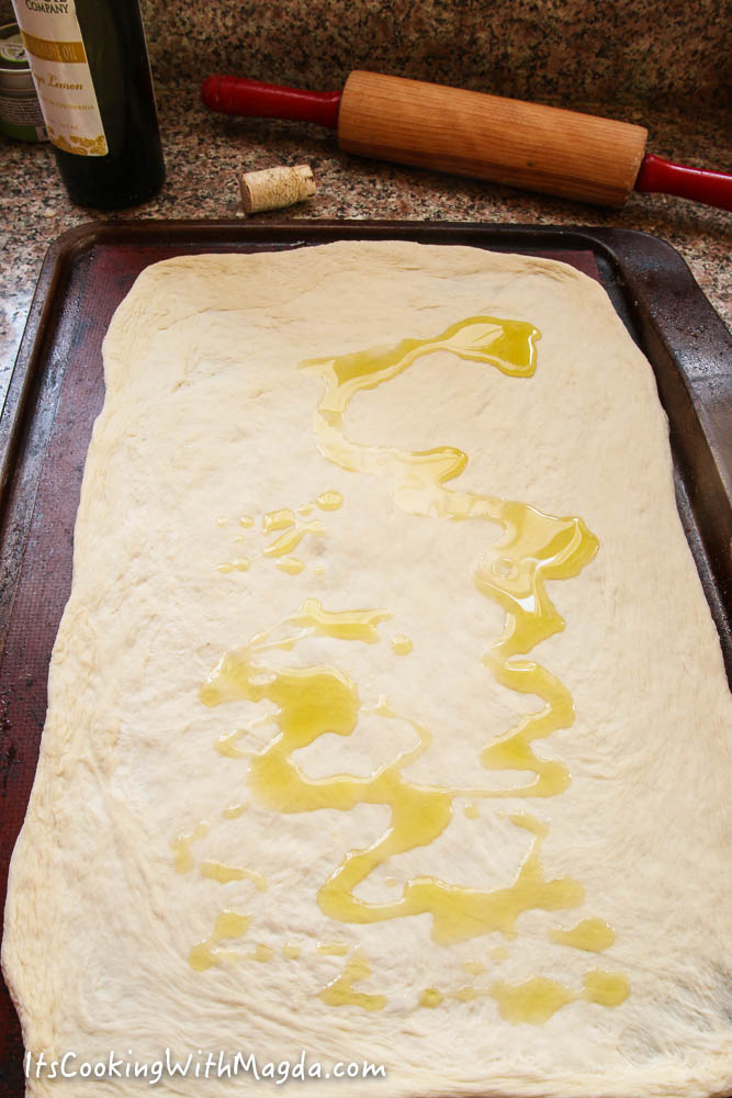 pizza dough on a baking sheet with olive oil drizzled