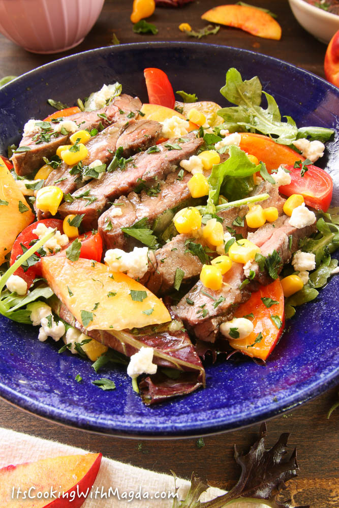 sliced skirt steak on top of greens, corn and nectarine