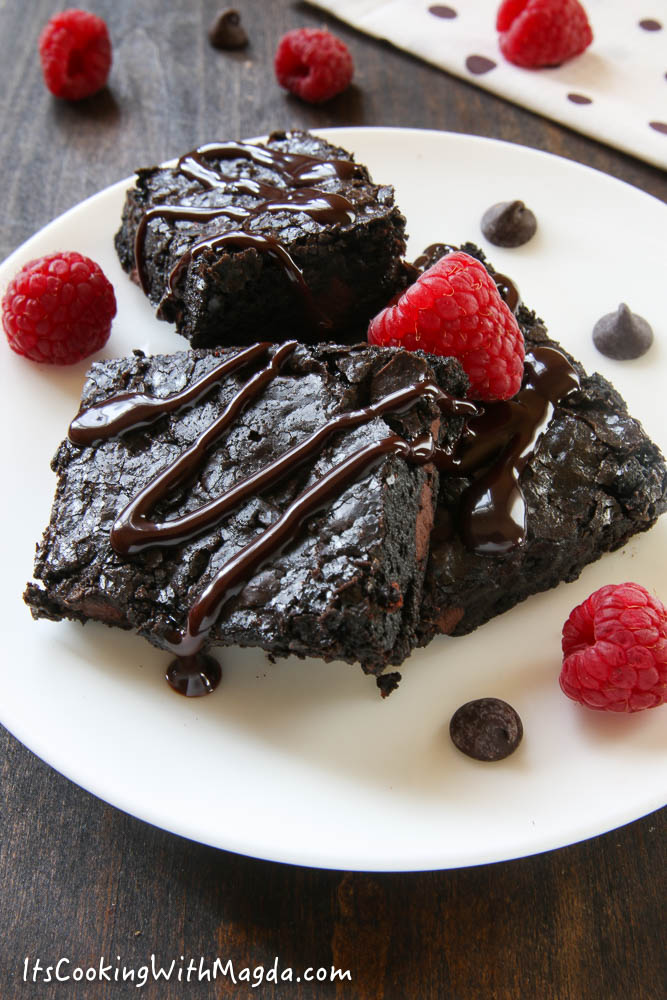 gooey brownies on a white plate decorated with raspberries